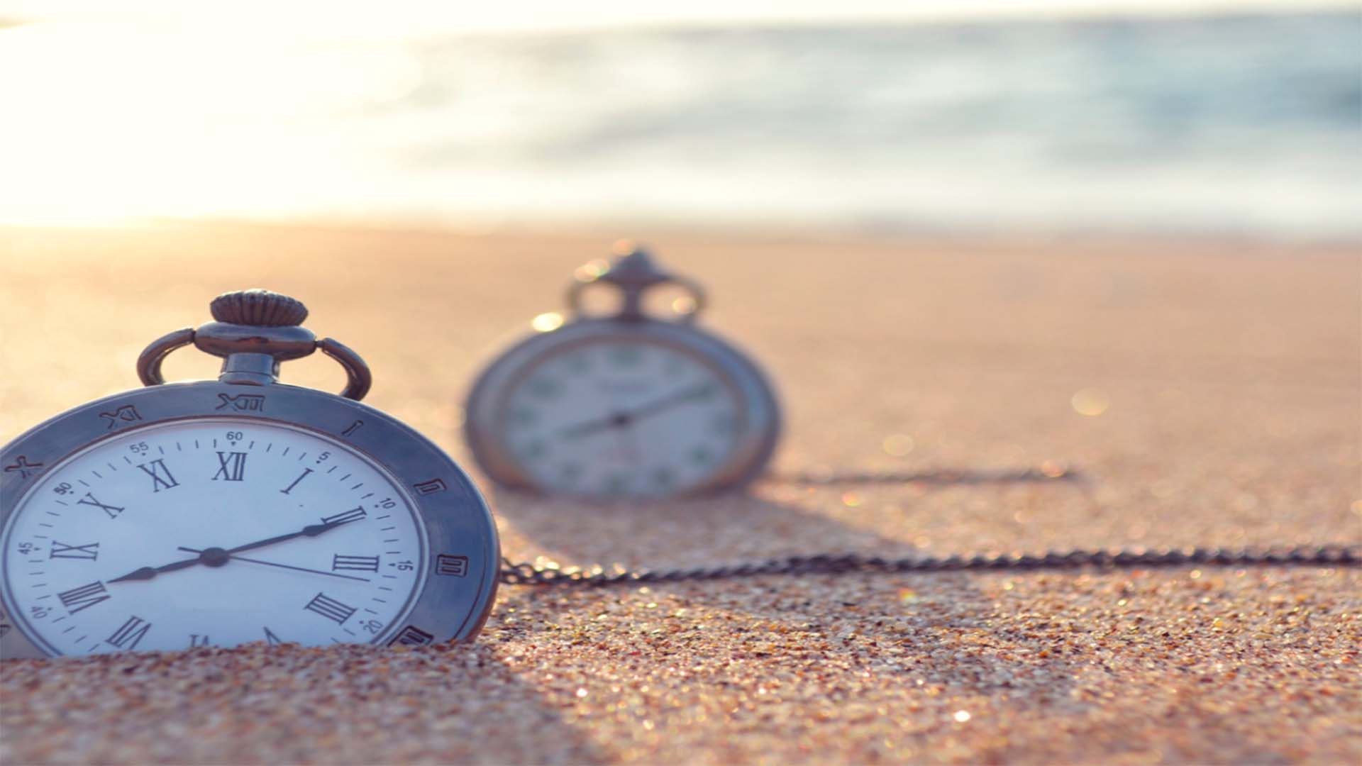 imagen de gestionar el tiempo en la que salen dos relojes de bolsillo en la arena de la playa con las olas de fondo